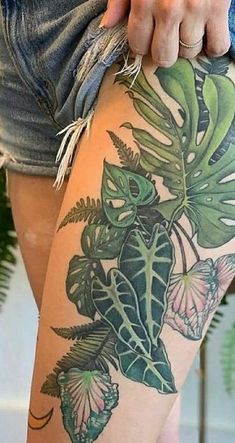 a woman's thigh with tattoos on her legs and some plants in the background