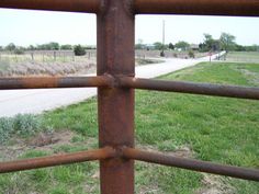 an old rusted metal fence in the middle of a grassy field next to a road