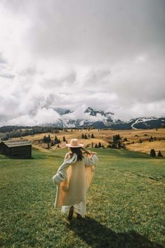 a woman standing on top of a lush green field next to a mountain covered in clouds