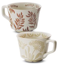 two coffee cups sitting next to each other on a white surface with leaves painted on them