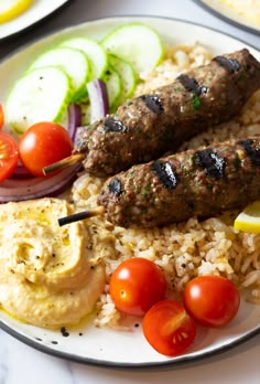 two kebabs on skewers over rice with tomatoes and cucumbers