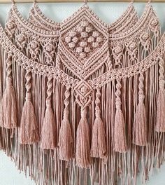 crocheted wall hanging with tassels and beads in pink tones on a white background