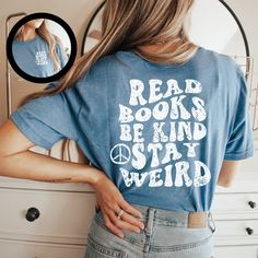 a woman standing in front of a mirror wearing a blue shirt that reads read books be kind of weird