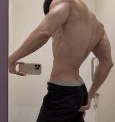 a shirtless man taking a selfie in front of a mirror with his cell phone