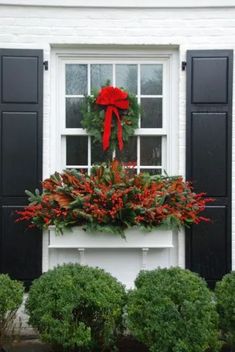 a christmas wreath on the window sill in front of a white house with black shutters