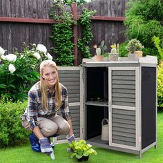 a woman kneeling down next to a potted plant on the grass in front of a shed