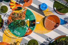 an aerial view of colorful chairs and tables in a park with trees on each side