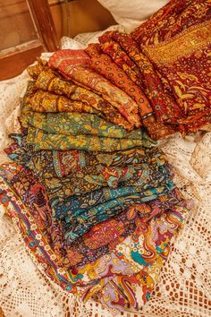 a pile of colorful scarves sitting on top of a white lace covered table cloth