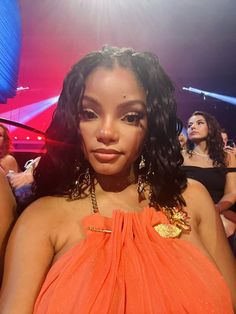 a close up of a person wearing an orange dress at a party with other people in the background