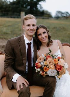 a bride and groom sitting on an old couch smiling at the camera with their bouquet in hand