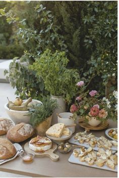 an assortment of breads, pastries and flowers on a picnic table in the sun