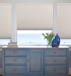 a blue dresser with two vases on top of it in front of large windows