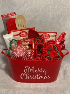 a red bucket filled with lots of christmas treats and candy canes next to a wooden spoon