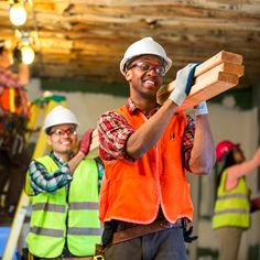 two men in safety vests and hard hats holding wooden planks while standing next to each other