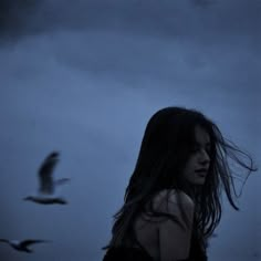 a woman with long hair standing in front of a flock of birds on a cloudy day