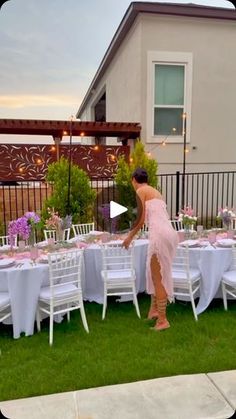 a woman in a pink dress standing at a table with white clothed tables and chairs