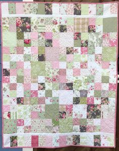 a pink and green patchwork quilt hanging on a wall