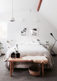 a bedroom with white walls and carpeted flooring is pictured in this image, there are plants on the table next to the bed