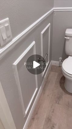 a white toilet sitting inside of a bathroom next to a wall mounted light switch and wooden flooring