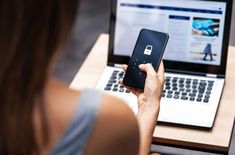 a woman is using her cell phone while sitting in front of a laptop with a padlock on the screen