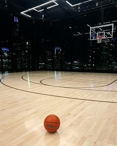 an indoor basketball court with a basket ball on the floor and city lights in the background