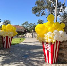 two buckets filled with yellow and white balloons sitting in front of a brick wall