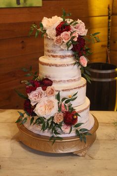 a three tiered wedding cake with red and pink flowers on the top, sitting on a gold platter