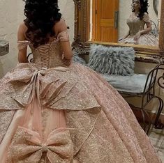 a woman in a ball gown is looking at herself in the mirror while wearing a large bow