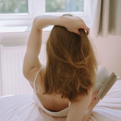 a woman laying on top of a bed with her hair blowing in the wind while reading a book