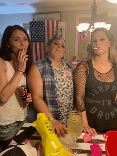 four women standing around a table with food and drinks in front of them, all looking at the camera