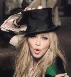 a woman with long blonde hair wearing a black top hat and posing for the camera