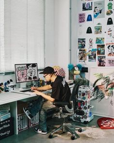 a young man sitting at a desk in front of a laptop computer on top of a white desk