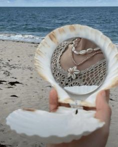 a person holding up a seashell on the beach with their reflection in it's shell