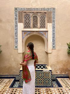 a woman standing in front of a wall with an arch and tile work on it