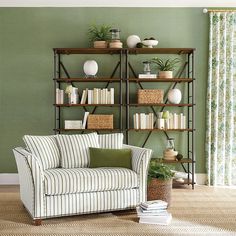 a living room with green walls and striped couch in front of a bookshelf