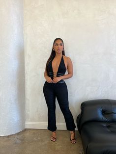 a woman standing next to a black couch in front of a white wall with her hands on her hips