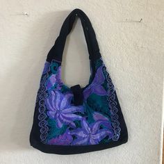 a purple and black purse hanging on a wall next to a white wall with a plant in it