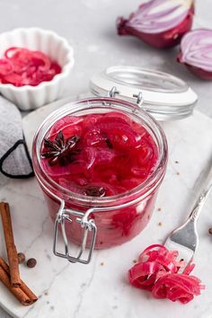 a jar filled with red liquid sitting on top of a white plate next to two spoons