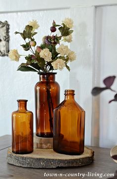 three brown vases with flowers in them sitting on a wooden table next to a mirror