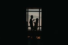 the silhouette of two people standing next to each other in front of an open window