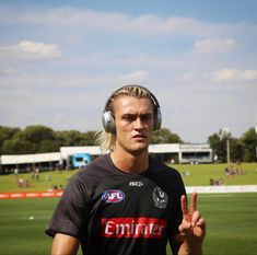 a man with headphones on giving the peace sign in front of a soccer field