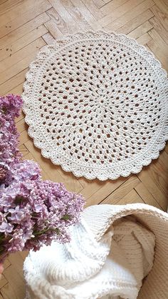 two crocheted doily sitting on top of a wooden floor next to purple flowers