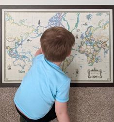 a young boy is looking at a map on the wall with his hands in it