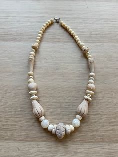 a white necklace with shells and beads on a wooden surface, the bead is attached to an adjustable clasp