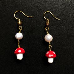 two red and white mushrooms are hanging from gold earwires on a black surface