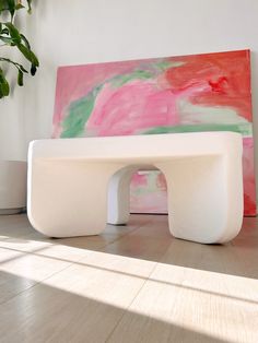 a white bench sitting on top of a hard wood floor next to a large painting