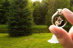 a person holding up a ring to take a photo in front of some pine trees