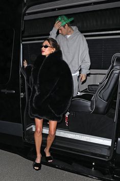 a woman in a fur coat stepping out of a vehicle with a man standing next to her