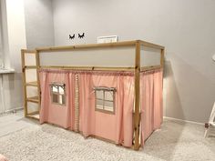 a doll house with pink curtains on the front and side walls, sitting in a white room