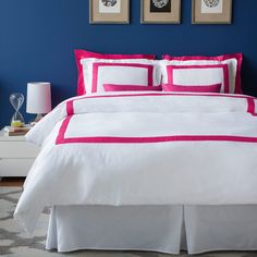 a bedroom with blue walls and white bedding, pink trim on the comforter